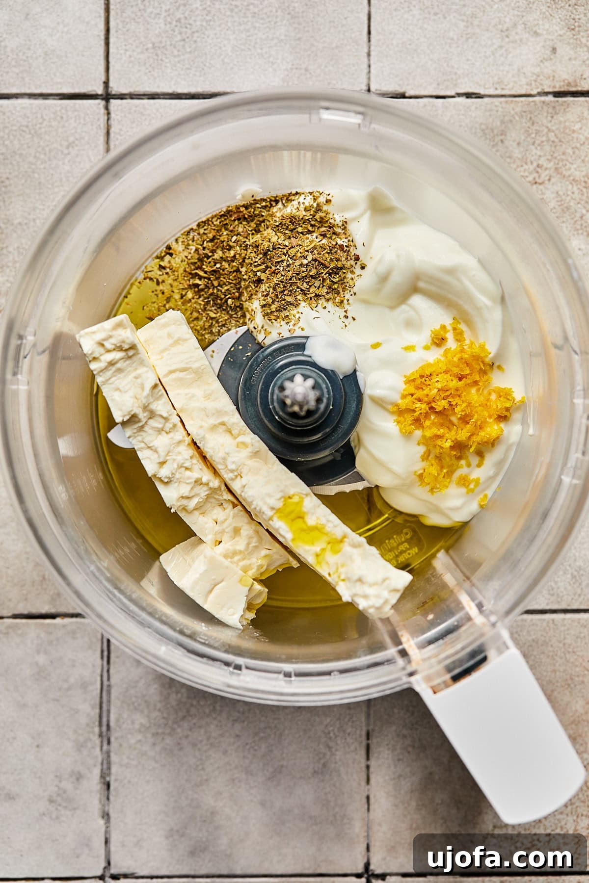 Ingredients for whipped feta—block feta, Greek yogurt, lemon zest, Italian seasoning, and olive oil—ready in a food processor.