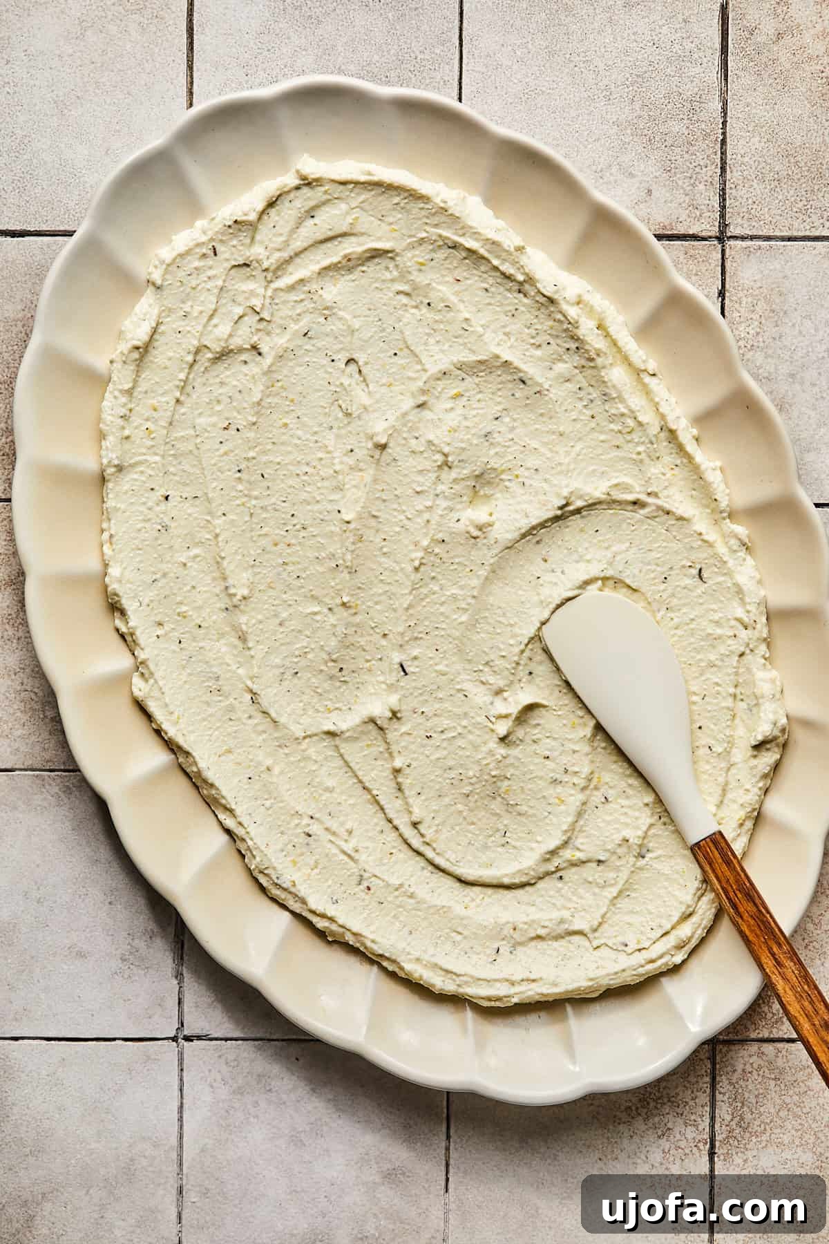 A smooth, thin layer of whipped feta spread evenly on a white serving platter, forming the base of the dip.