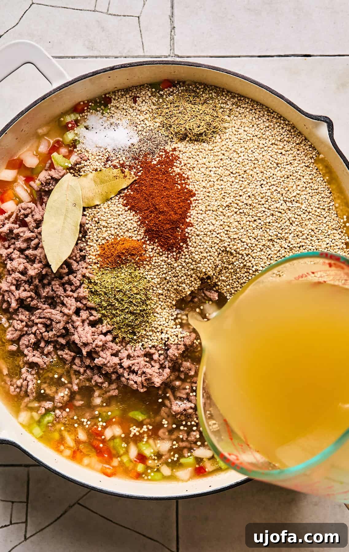 Dirty Quinoa: A Flavorful and Healthy Take on a Classic 6 Uncooked quinoa, cooked ground beef, chicken broth, bay leaves, and spices being added to the sautéed vegetables in the skillet.