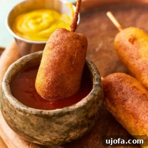 A gluten-free corn dog dipped in ketchup, showcasing its crispy texture.