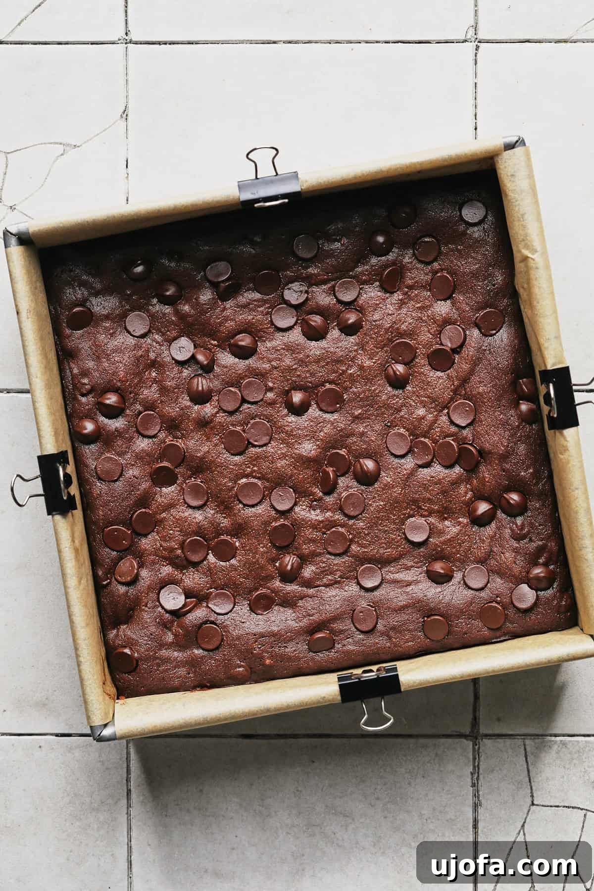protein brownies in a square baking pan lined with parchment paper and clips to hold the paper down.