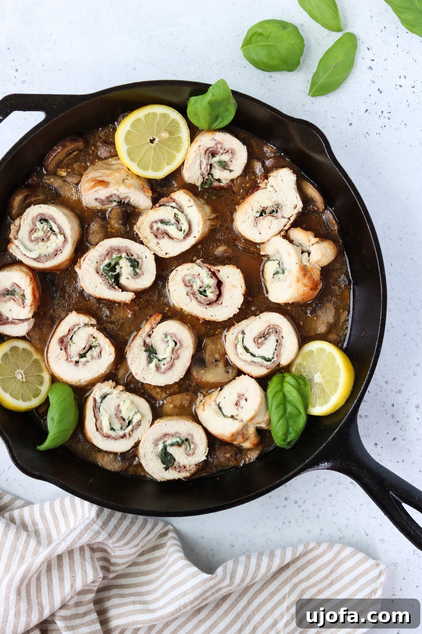 A plate of two prosciutto basil stuffed chicken rolls, sliced to reveal the filling, drizzled with the mushroom lemon sauce.