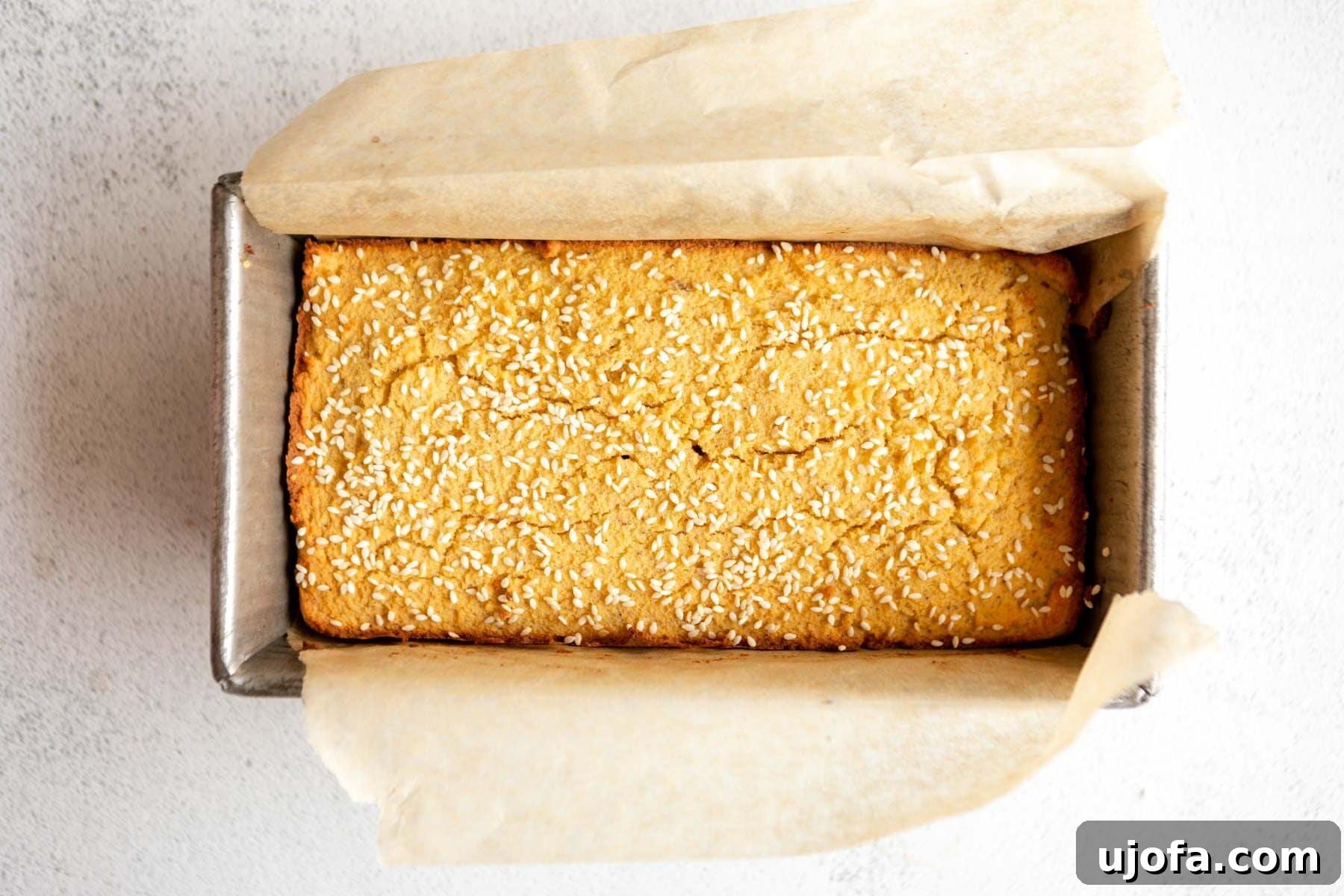 A freshly baked, golden-brown loaf of coconut flour bread, still in its parchment-lined loaf pan, cooling on a wire rack.