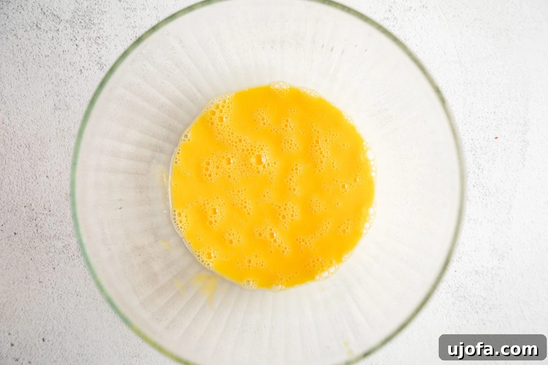 Five large eggs cracked into a clear glass mixing bowl, ready for beating.