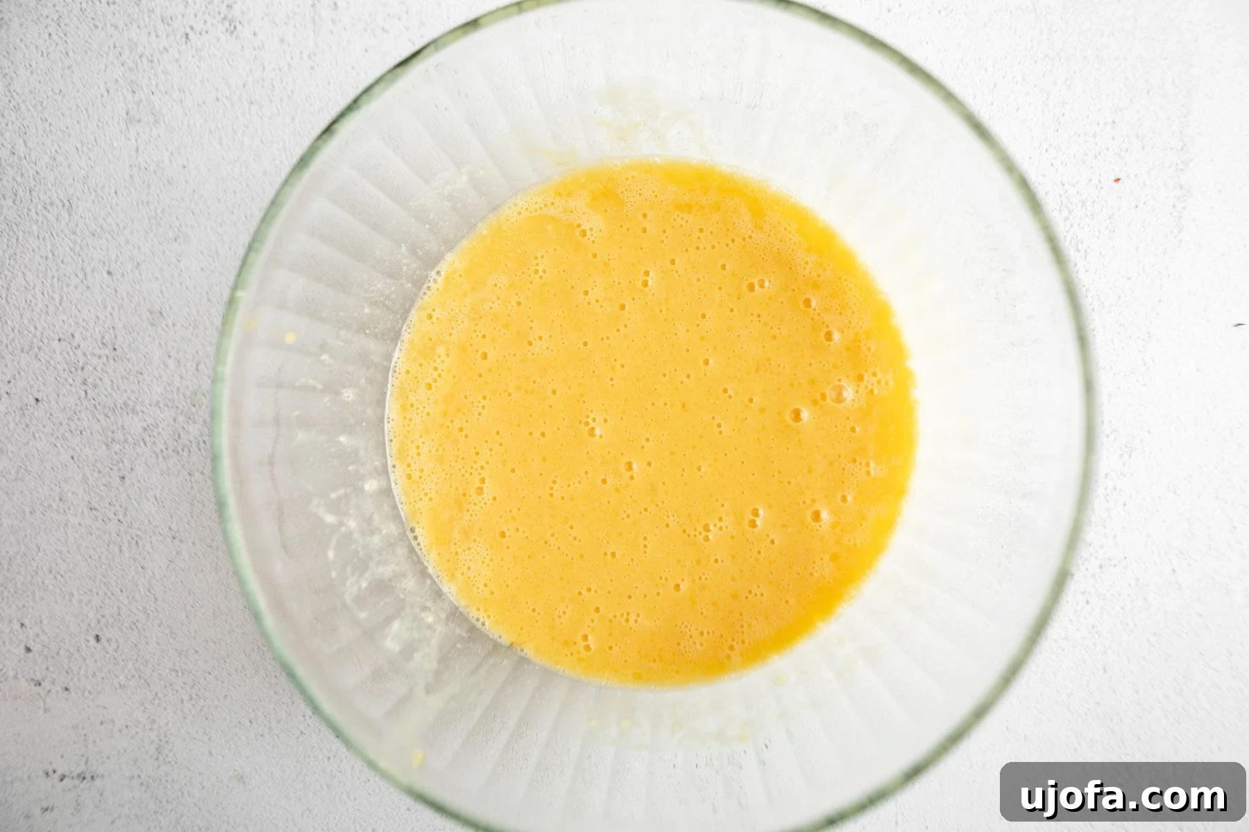 Beaten eggs in a clear glass bowl, appearing frothy and light yellow, indicating they are well-mixed.