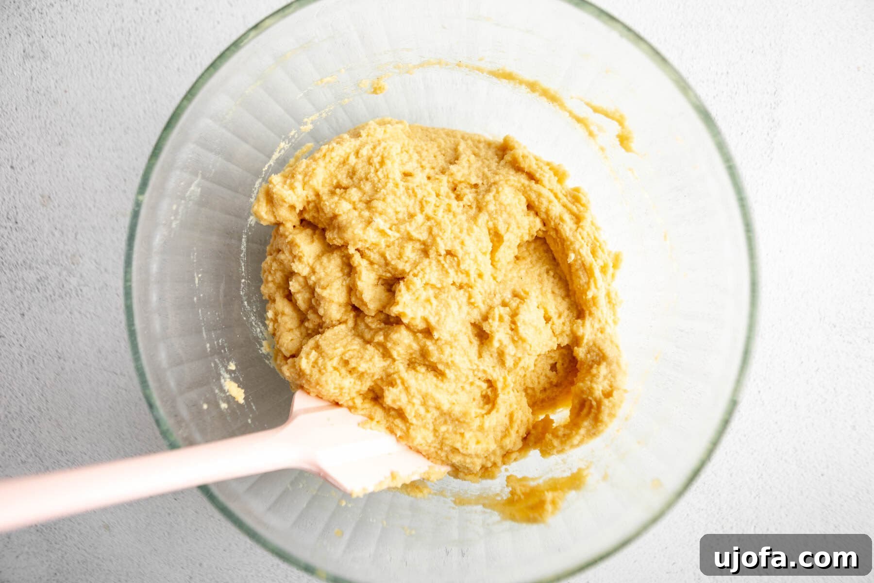 Thick, creamy coconut flour bread dough in a glass mixing bowl, with a rubber spatula resting inside it.