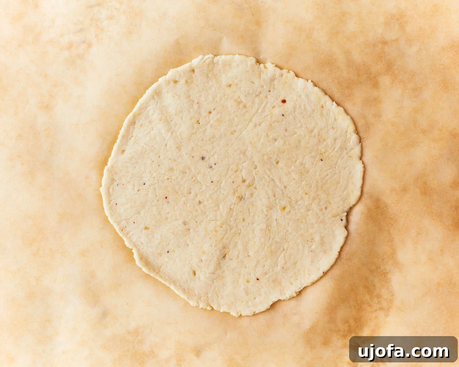 An almond flour tortilla dough circle on parchment paper, ready for cooking.