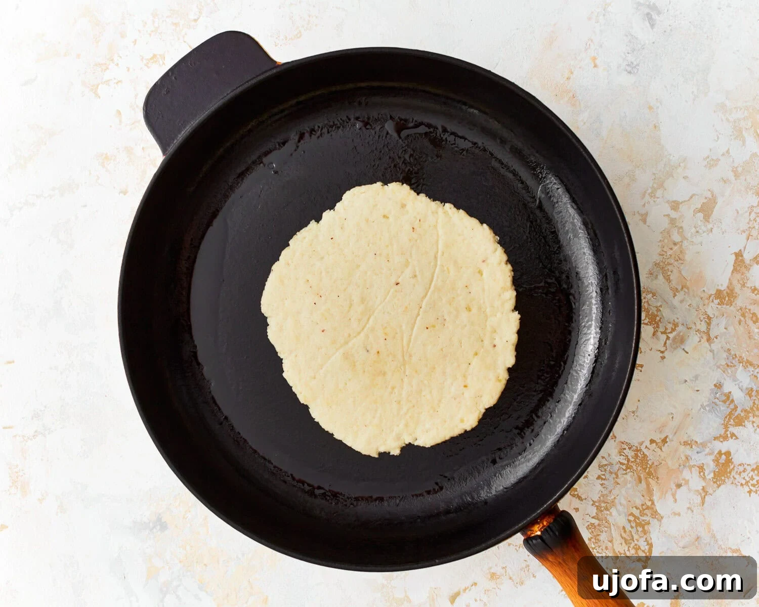 Overhead view of an almond flour tortilla cooking in a hot skillet, showing early browning.