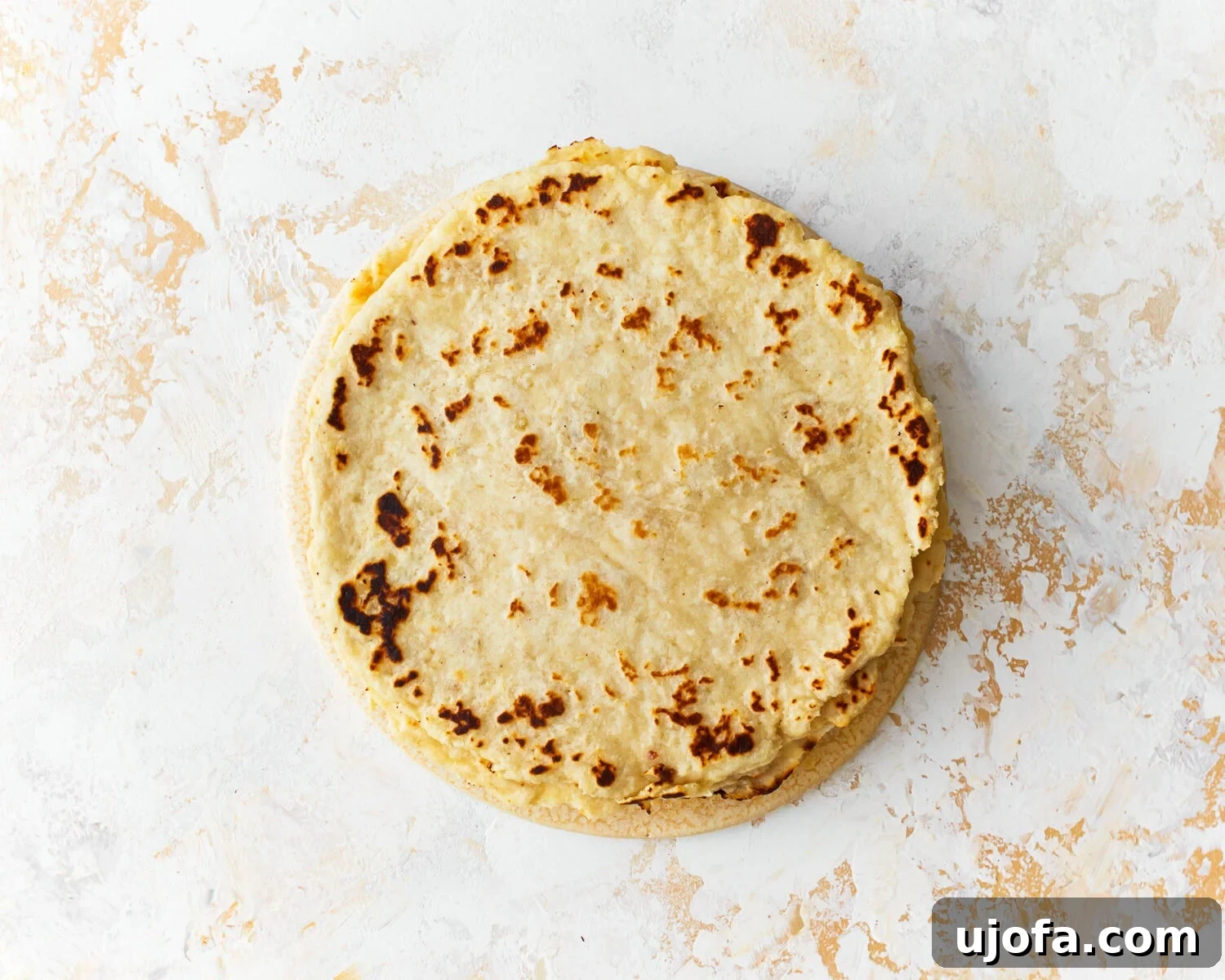 A completed stack of warm almond flour tortillas, covered with a kitchen towel.
