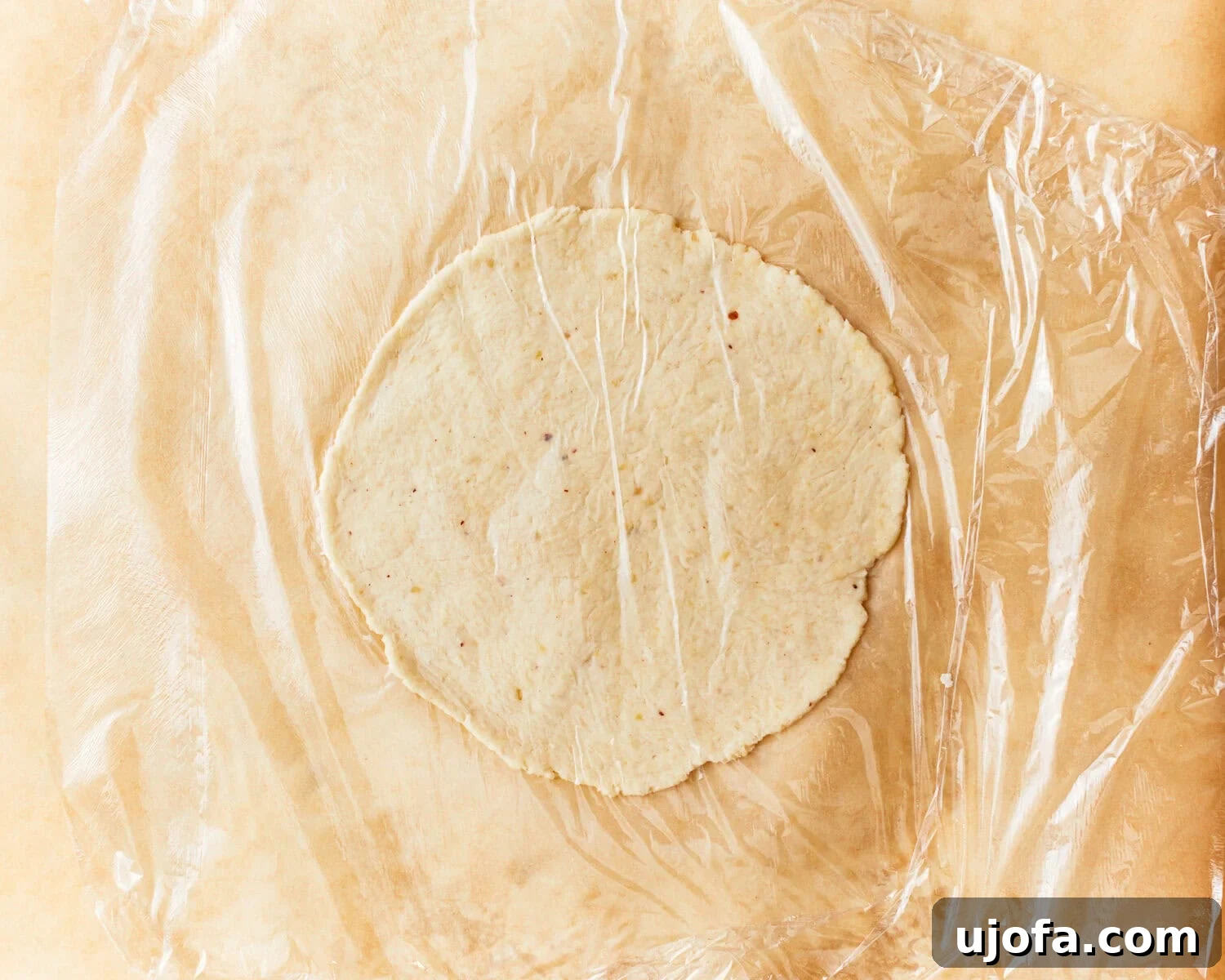 One portion of almond flour tortilla dough rolled out between two sheets of parchment paper.