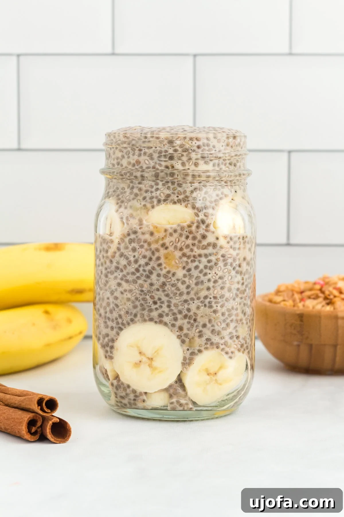 A side view of a serving of banana chia pudding in a clear mason jar, garnished with banana slices and a sprinkle of cinnamon.