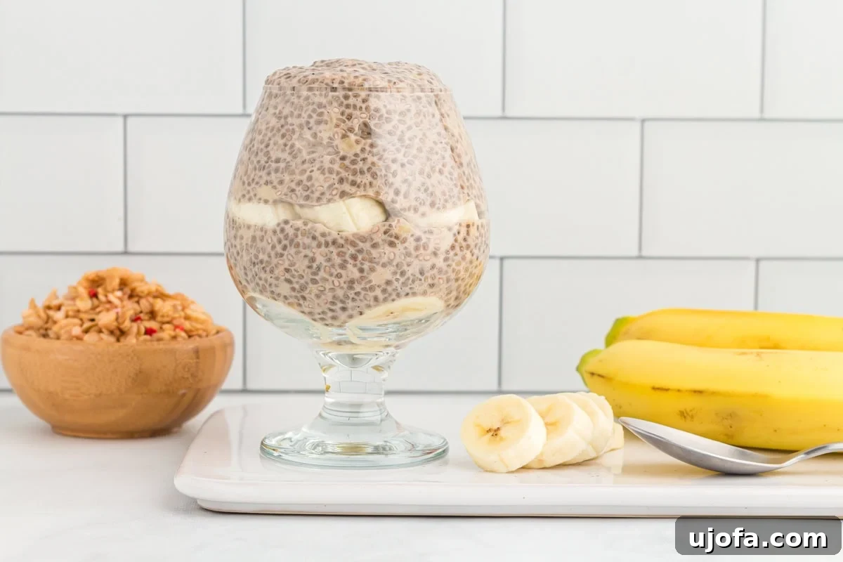 A side view of banana chia pudding served in an elegant stemmed glass, showing layers of creamy pudding, topped with fresh banana slices.