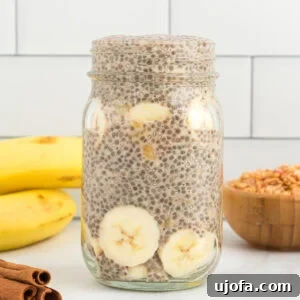 A side view of a serving of banana chia pudding in a clear mason jar, garnished with banana slices and a sprinkle of cinnamon.