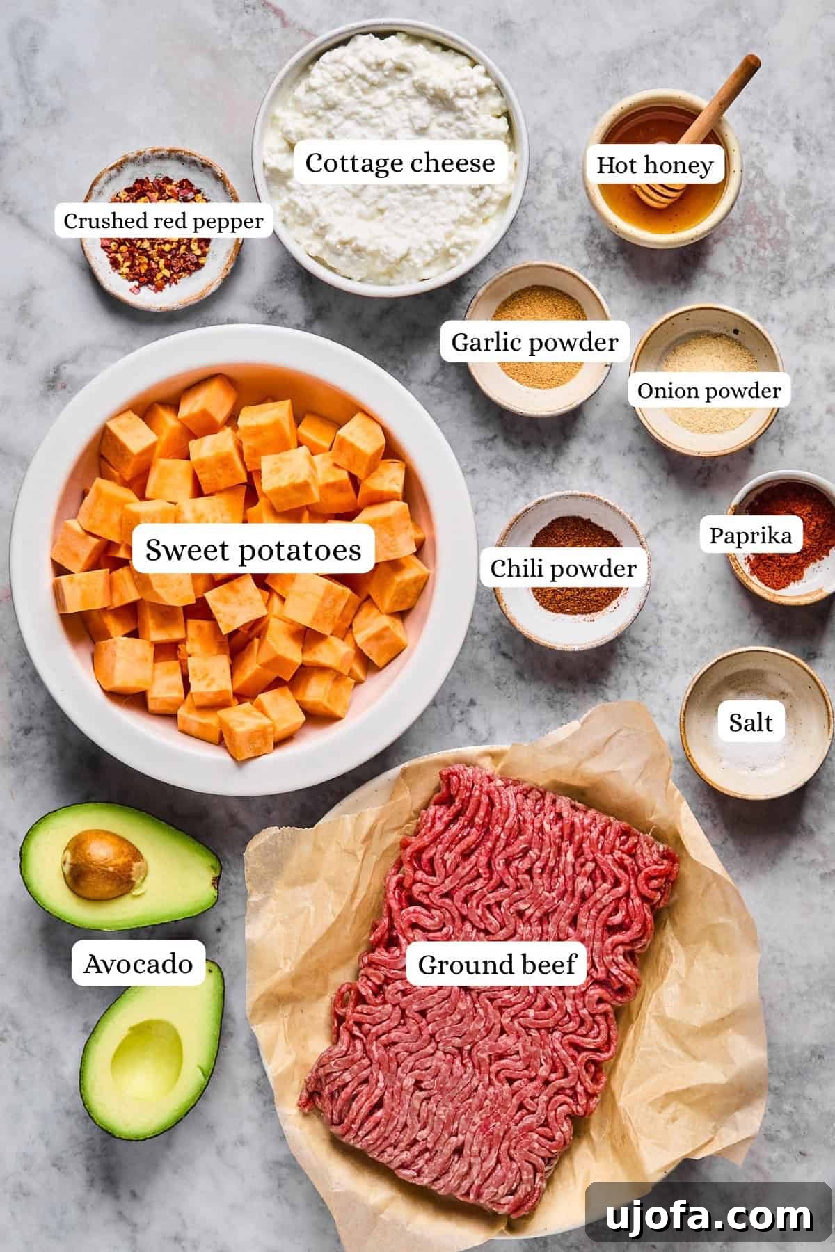 Image displaying a selection of fresh ingredients: a bowl of diced sweet potatoes, a container of creamy cottage cheese, uncooked ground beef, a sliced avocado, and small bowls filled with aromatic spices like crushed red pepper, hot honey, paprika, salt, chili powder, garlic powder, and onion powder.