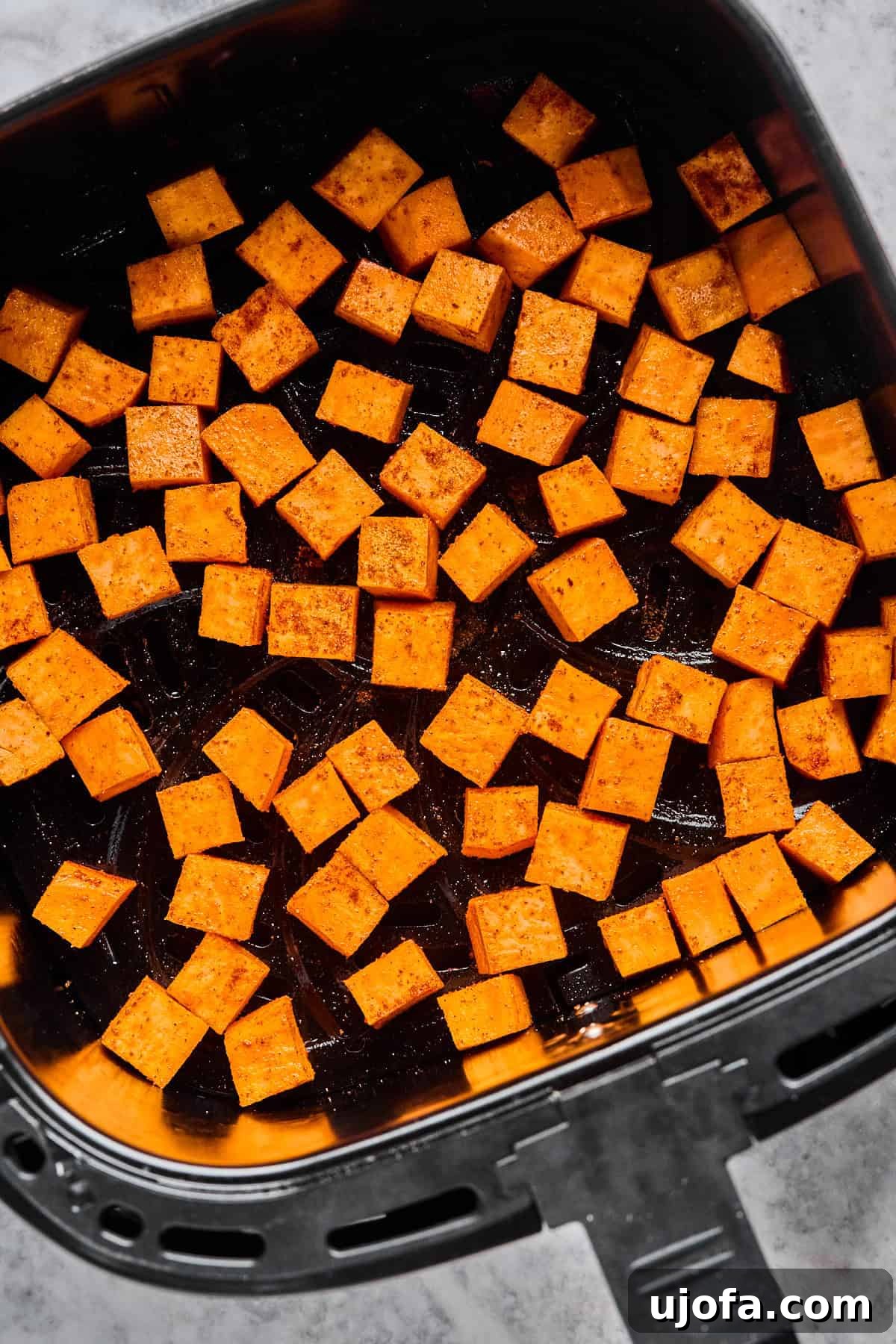 Diced sweet potato cubes cooking to golden perfection in an air fryer basket, ready to become a sweet and crispy base for the taco bowl.
