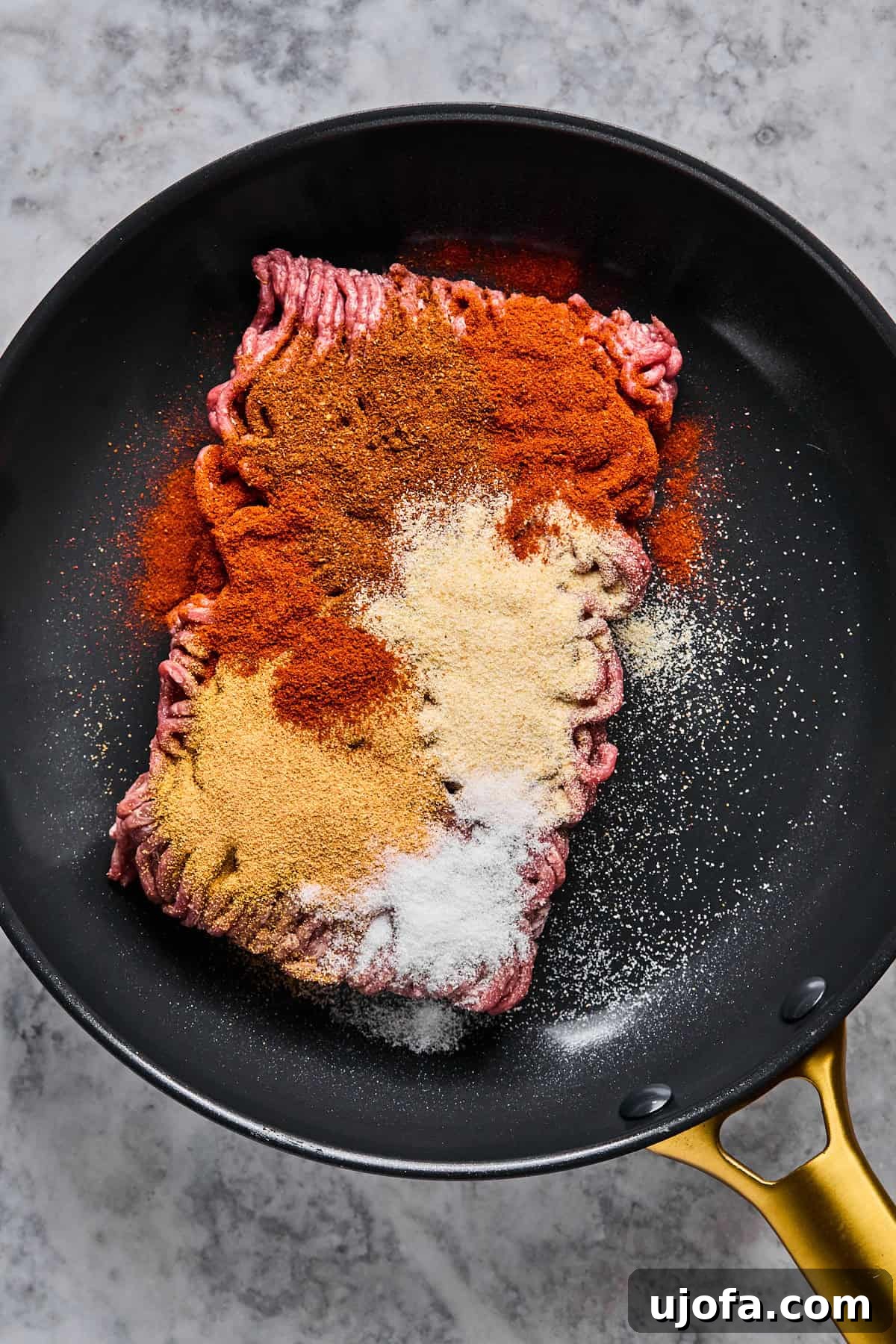Uncooked ground beef seasoned with a blend of spices in a hot skillet, ready to be browned for the taco bowl filling.