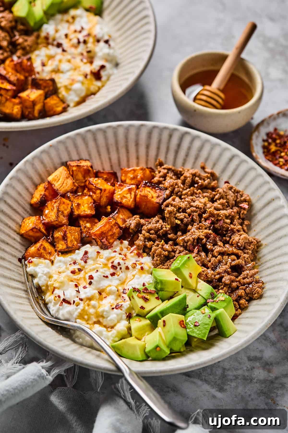 A beautifully assembled cottage cheese taco bowl, brimming with ground beef, avocado slices, roasted sweet potatoes, and a generous scoop of cottage cheese, artfully drizzled with hot honey and sprinkled with red pepper flakes.