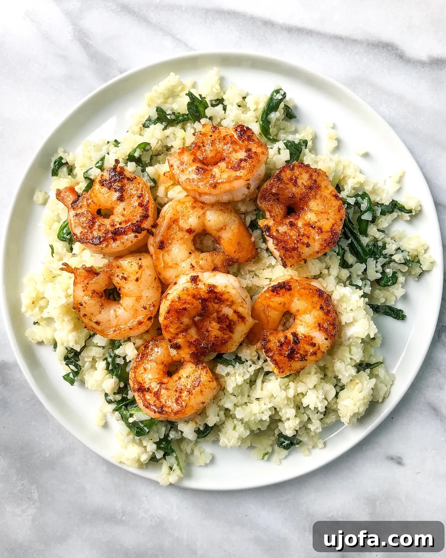 Spicy shrimp and creamy spinach cauliflower rice dish in a bowl, garnished with fresh herbs