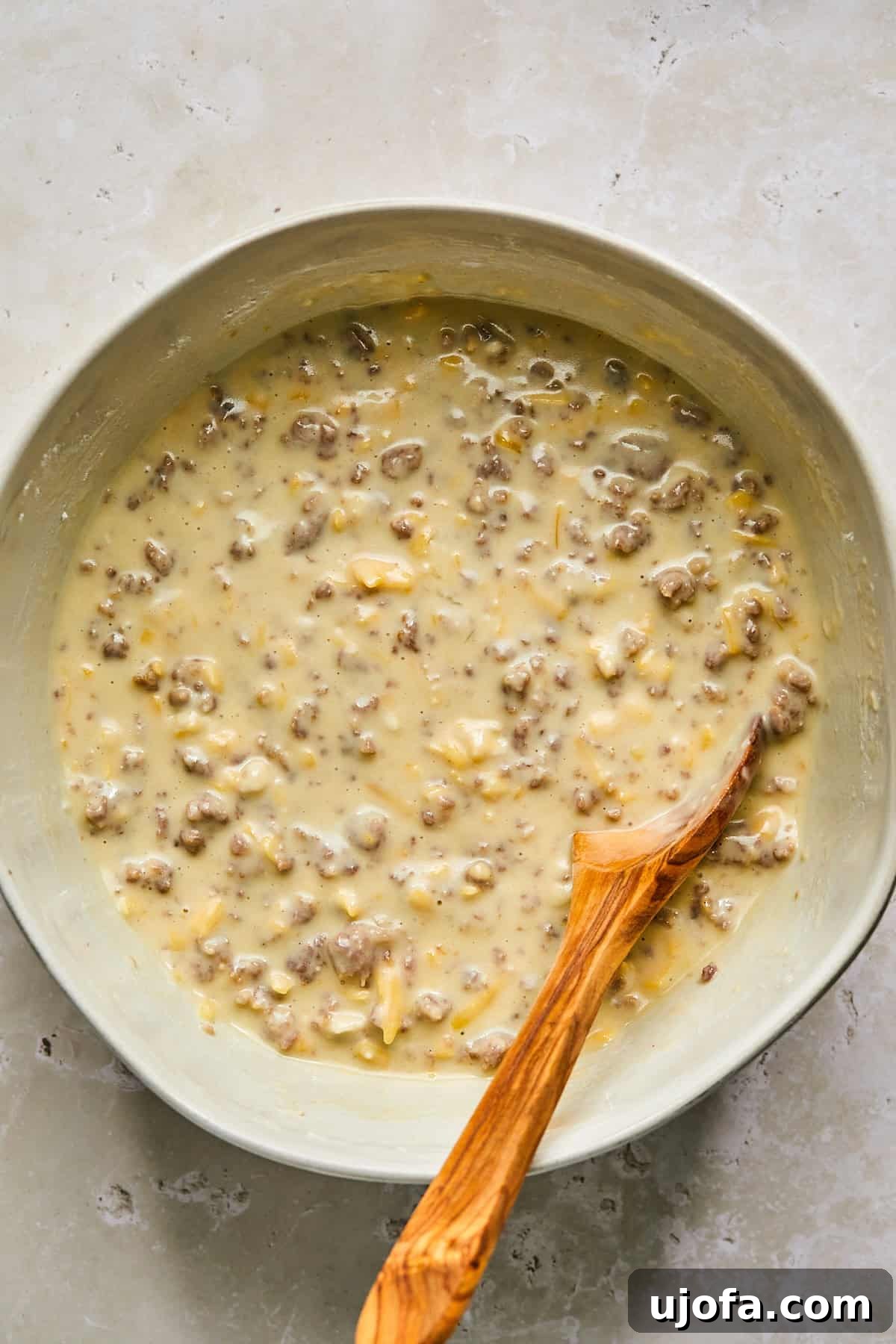 Mixing pancake batter with cheese, sausage, and maple syrup in a skillet