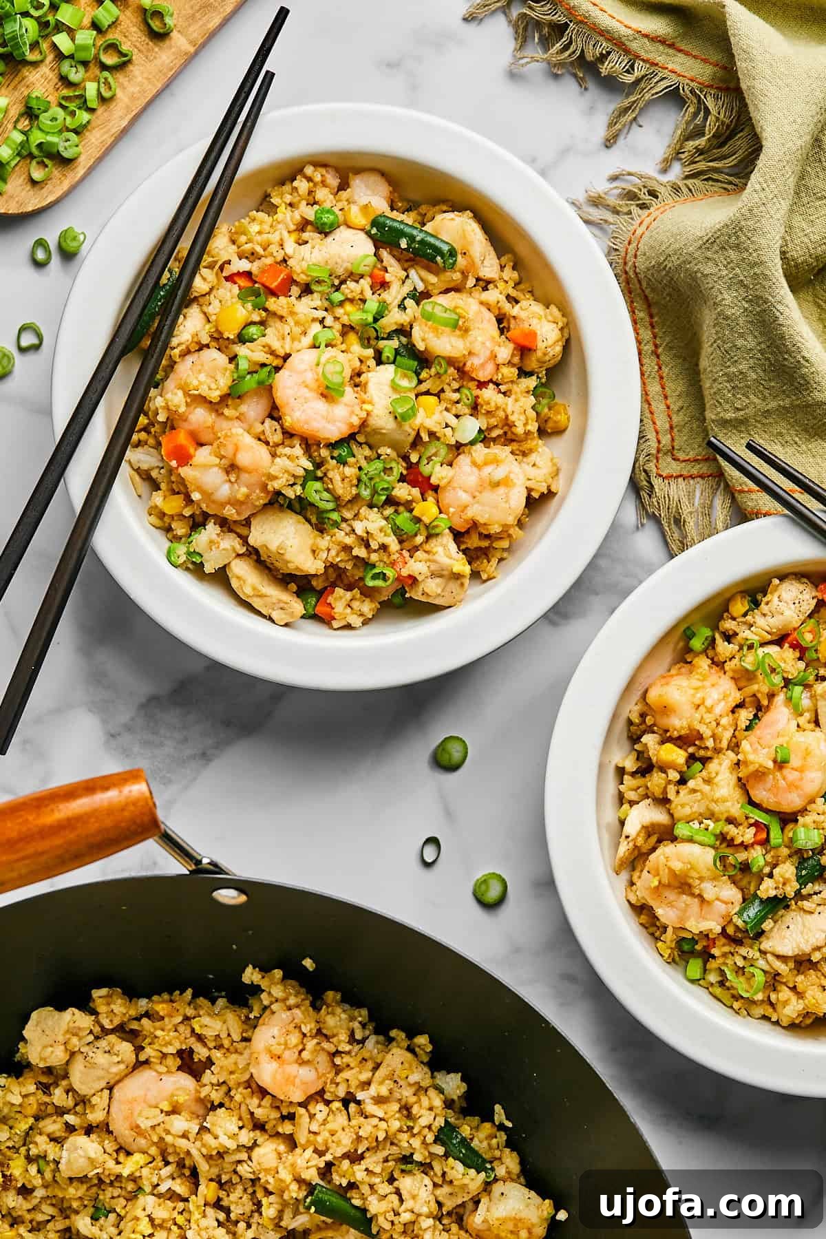 two bowls and a skillet of chicken and shrimp fried rice in a white bowl with green onions