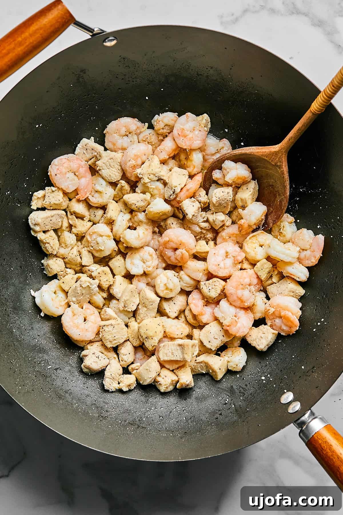 Chicken and shrimp cooking in a large skillet with sesame oil