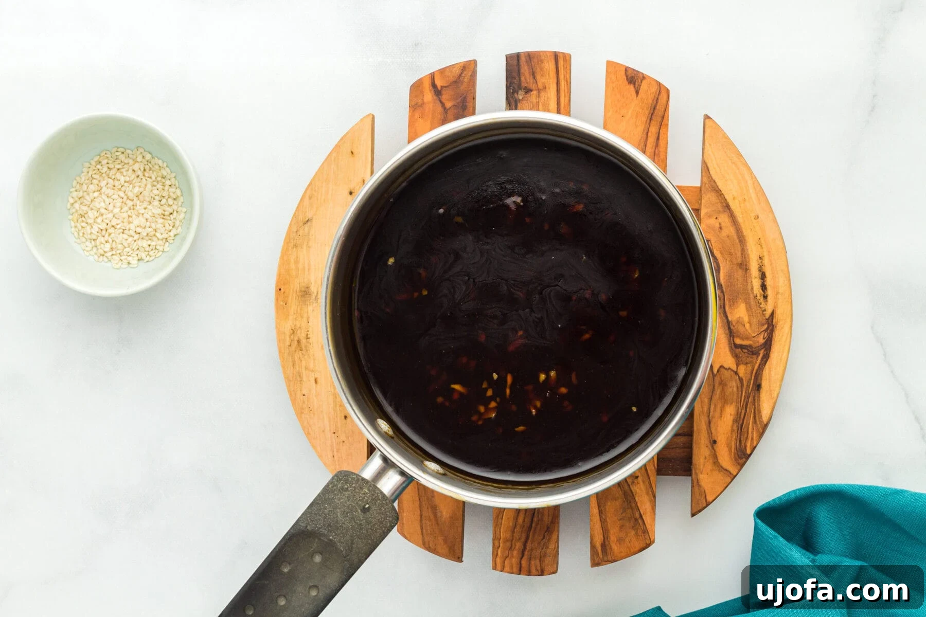 Overhead view of gluten free teriyaki sauce in a saucepan next to a bowl of sesame seeds.