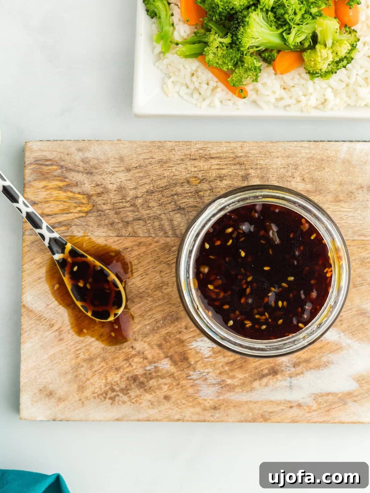 Overhead view of a glass jar filled with gluten free teriyaki sauce and a spoon on a wooden chopping board.