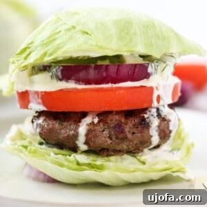 A beautifully plated Greek burger with all its fresh toppings and dairy-free tzatziki, presented on a rustic board.