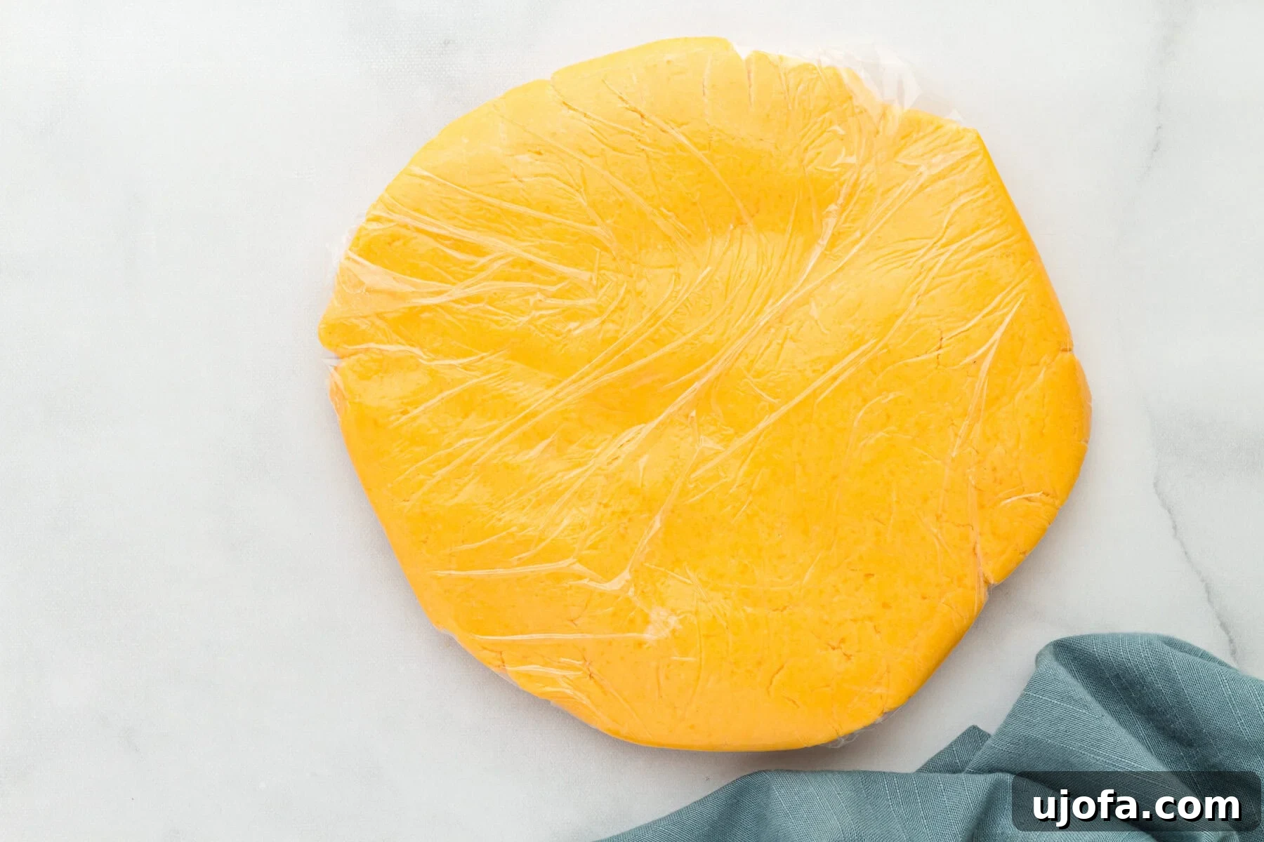 A flattened ball of gluten-free Cheez-Its dough wrapped in plastic wrap, ready for chilling.