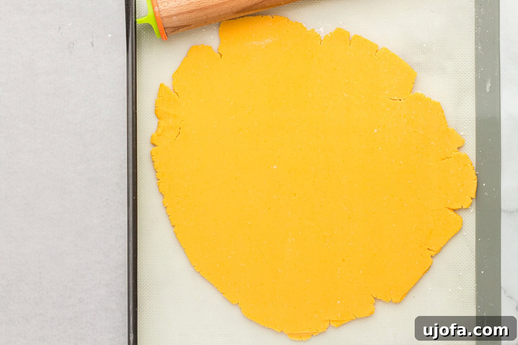 Rolled out gluten-free Cheez-Its dough on a silicone baking mat, ready for cutting.