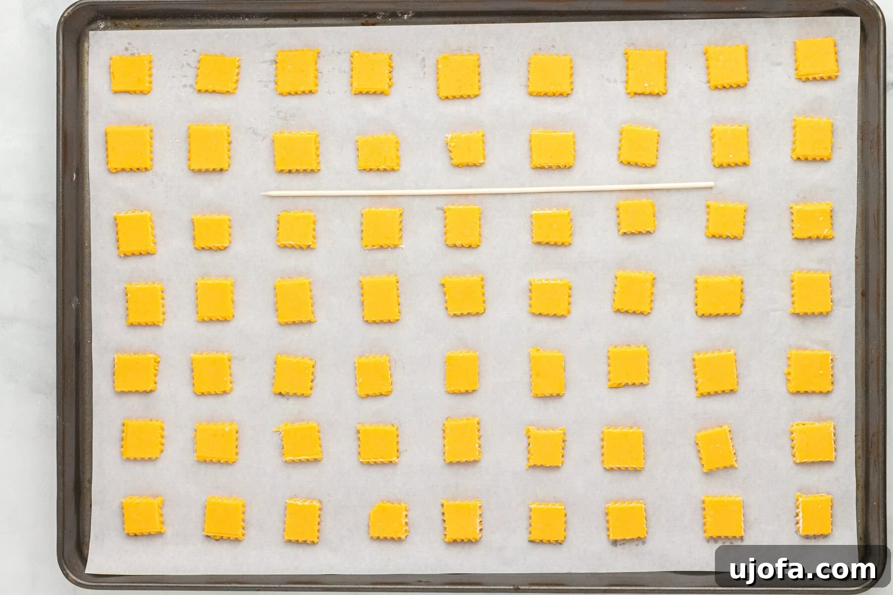 Uncooked gluten-free Cheez-Its squares arranged on a parchment-lined baking sheet.