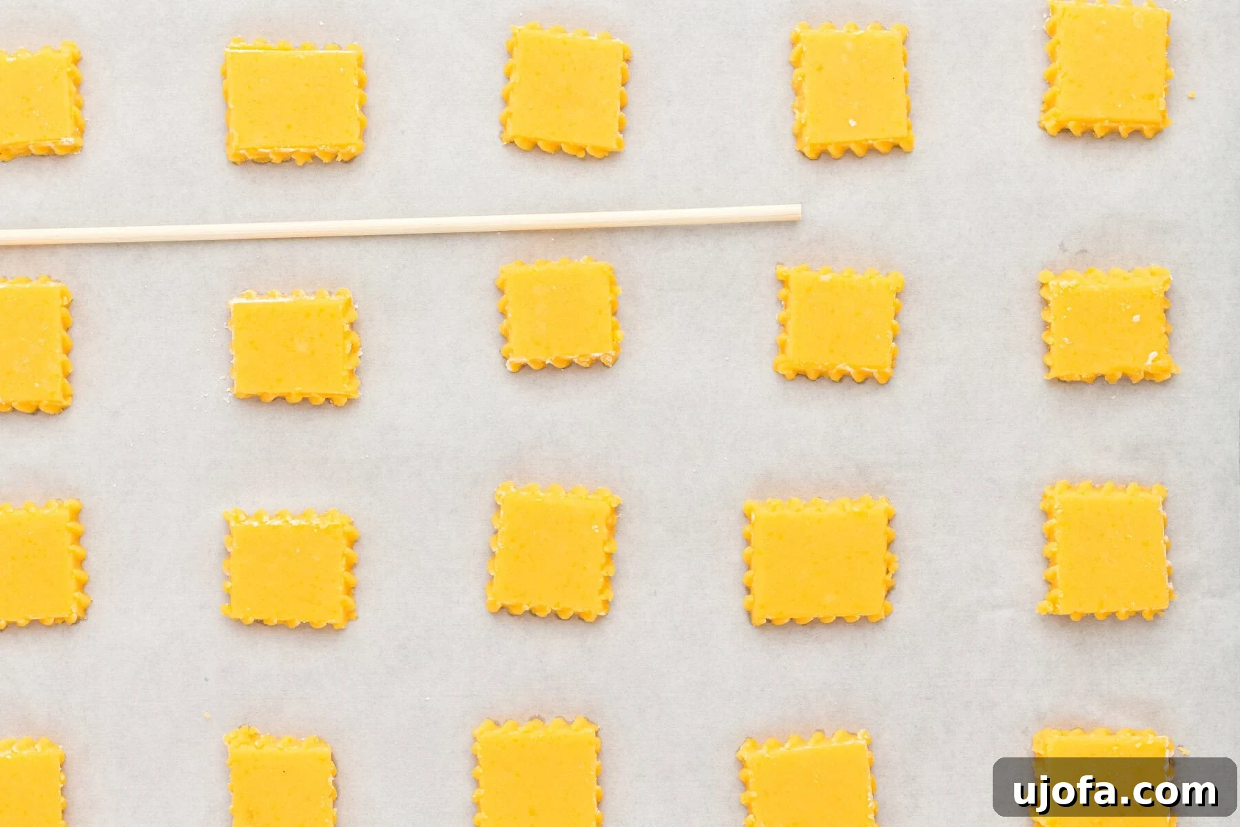 Uncooked gluten-free Cheez-Its on a baking sheet with a wooden skewer, showing the perforation step.