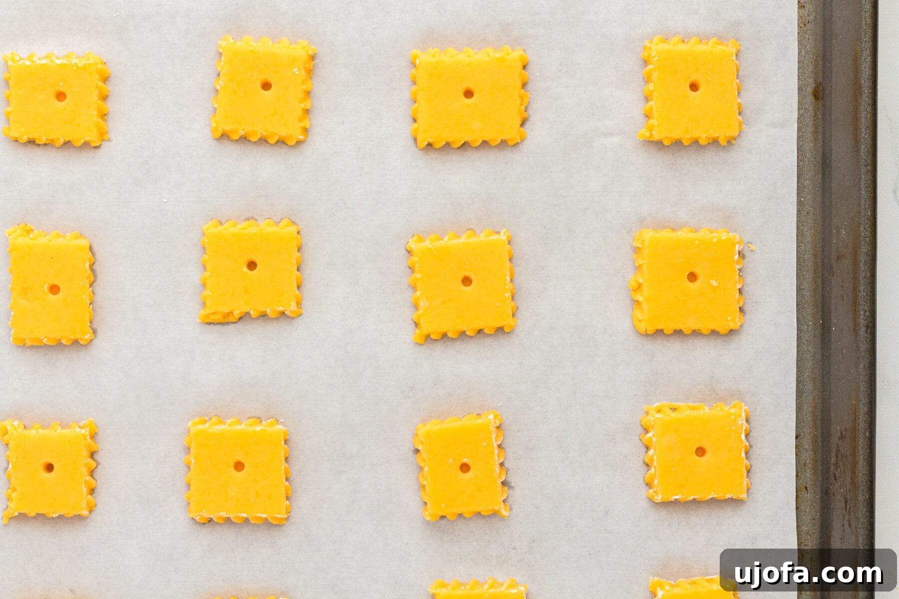 Overhead view of uncooked gluten-free Cheez-Its crackers on a parchment-lined baking sheet.