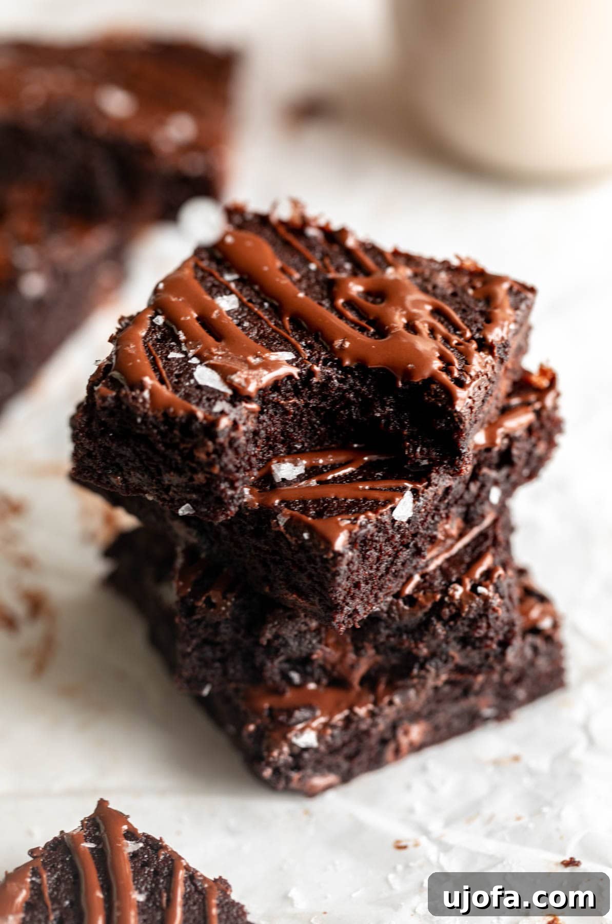 Fudgy Coconut Flour Brownies 2 A stack of coconut flour brownies, with a rich, dark brown color and a slightly crinkled top. They are stacked on a white plate with one brownie showing its fudgy interior.