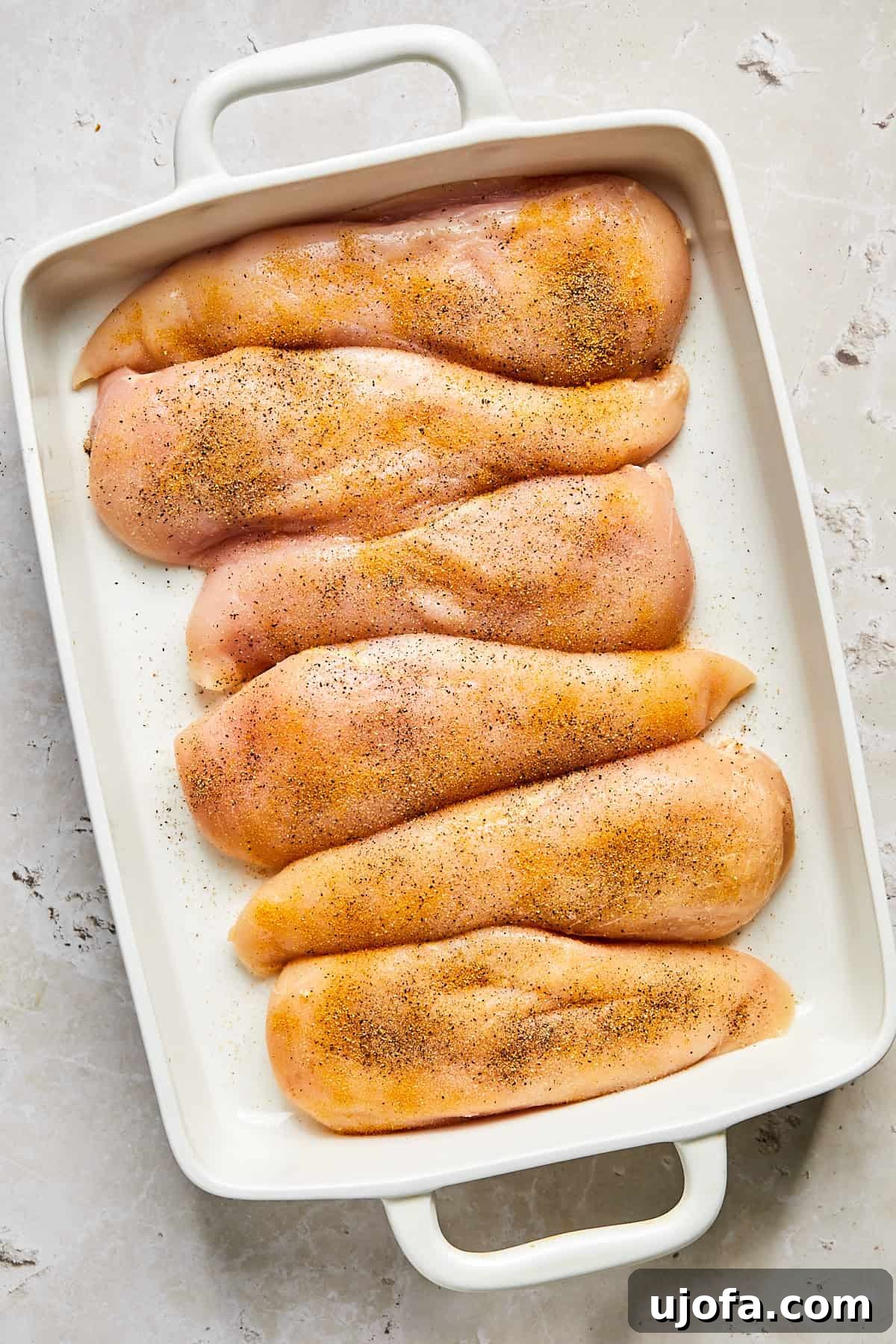 Raw chicken breasts seasoned in a baking dish, ready for the pesto topping