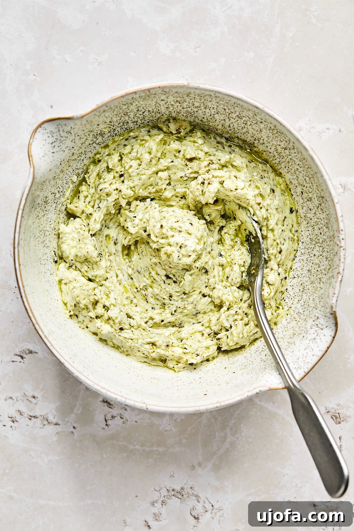 Cream cheese and pesto mixture being stirred together in a mixing bowl