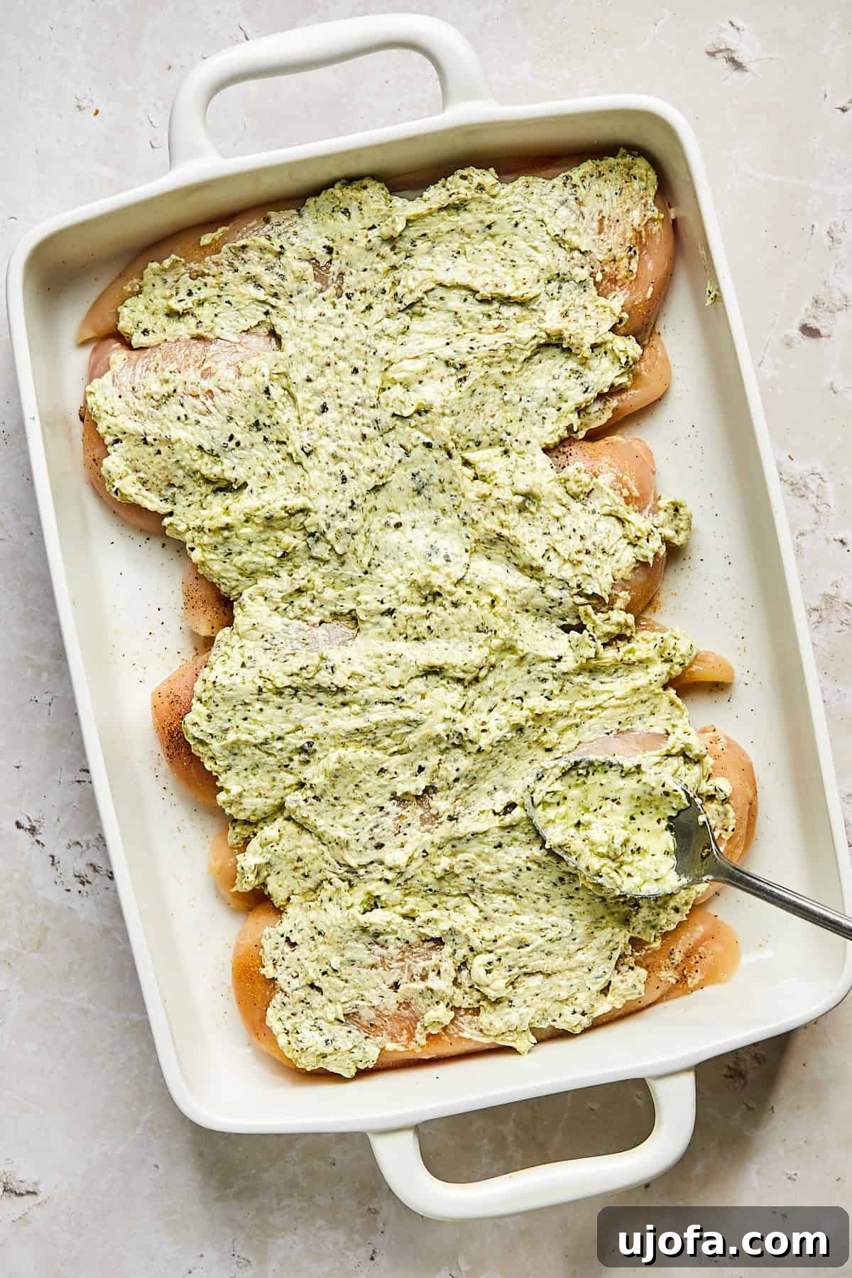 Pesto cream cheese mixture spread over seasoned chicken in a baking dish