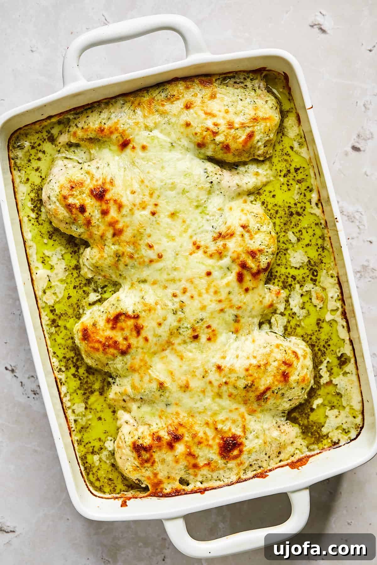 Baked pesto chicken with golden cheese topping and visible bubbling edges, fresh out of the oven