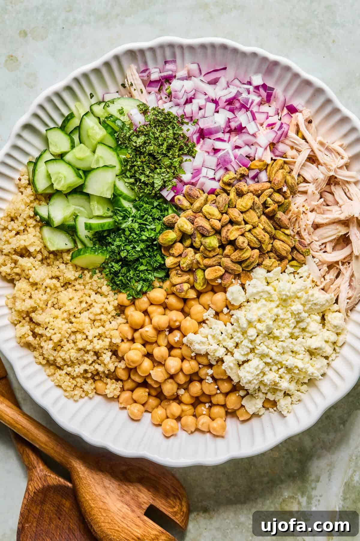 Jennifer Aniston Protein Power Prep Salad 5 Step 2: A large white mixing bowl filled with all the vibrant salad ingredients—quinoa, shredded chicken, chickpeas, cucumber, and fresh herbs—before dressing.