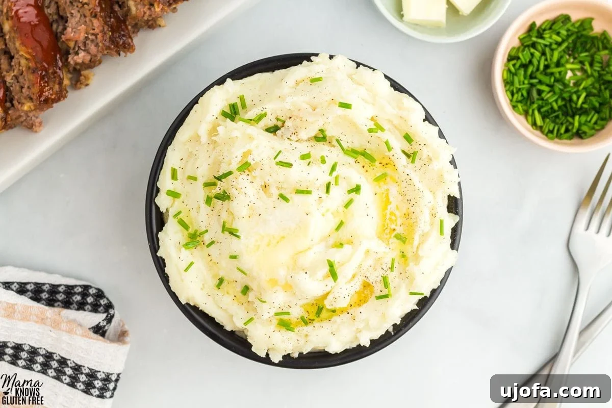 gluten-free mashed potatoes in a black bowl with forks, chives, butter, and meatloaf in the background.