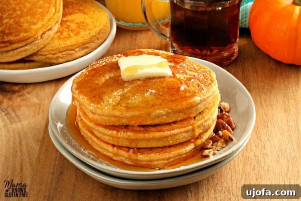 gluten-free pumpkin pancakes on a white plate with butter and syrup and more pancakes and syrup in the background