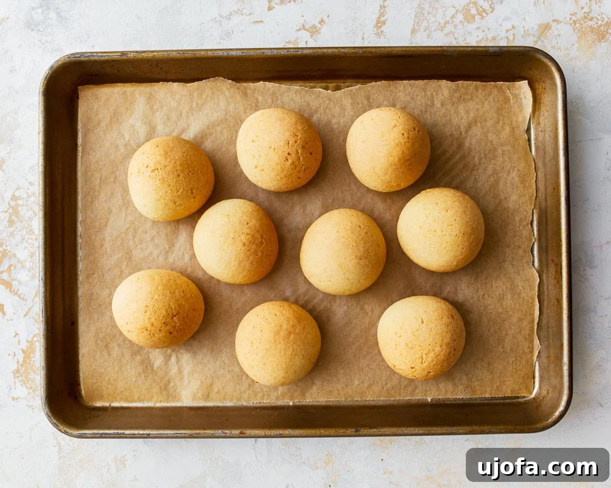 Golden Pandebono Colombian Bakery Classic 11 A batch of freshly baked, golden brown pandebono rolls cooling on a parchment lined baking sheet, steam gently rising.