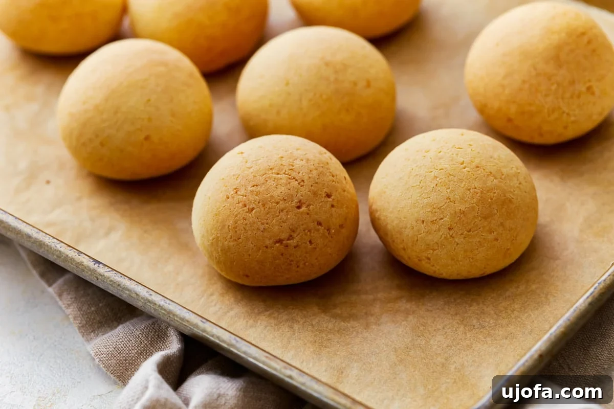 Golden Pandebono Colombian Bakery Classic 4 Side view of golden brown Pandebono rolls on a parchment lined baking sheet, showcasing their crispy crust and puffed texture, ready for serving.