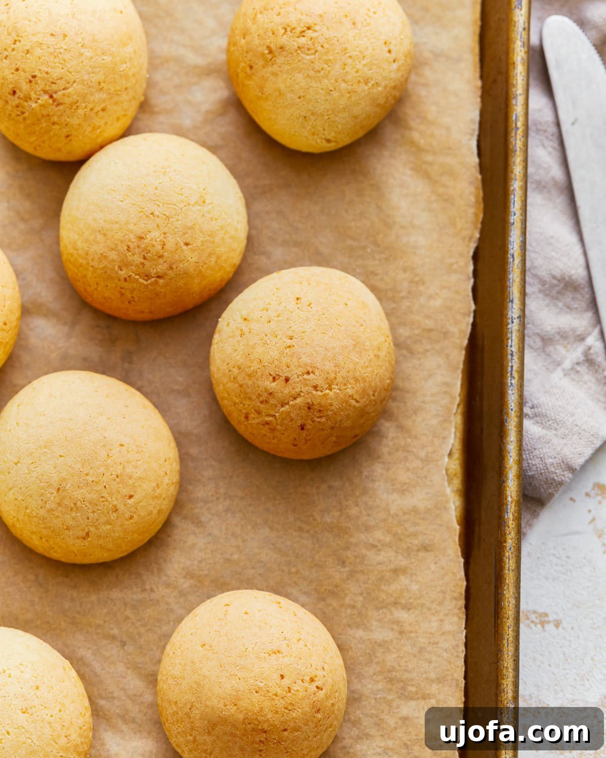 Golden Pandebono Colombian Bakery Classic 5 Overhead view of several Pandebono Colombian cheese bread rolls arranged on a parchment lined baking sheet, highlighting their rustic charm and golden finish.