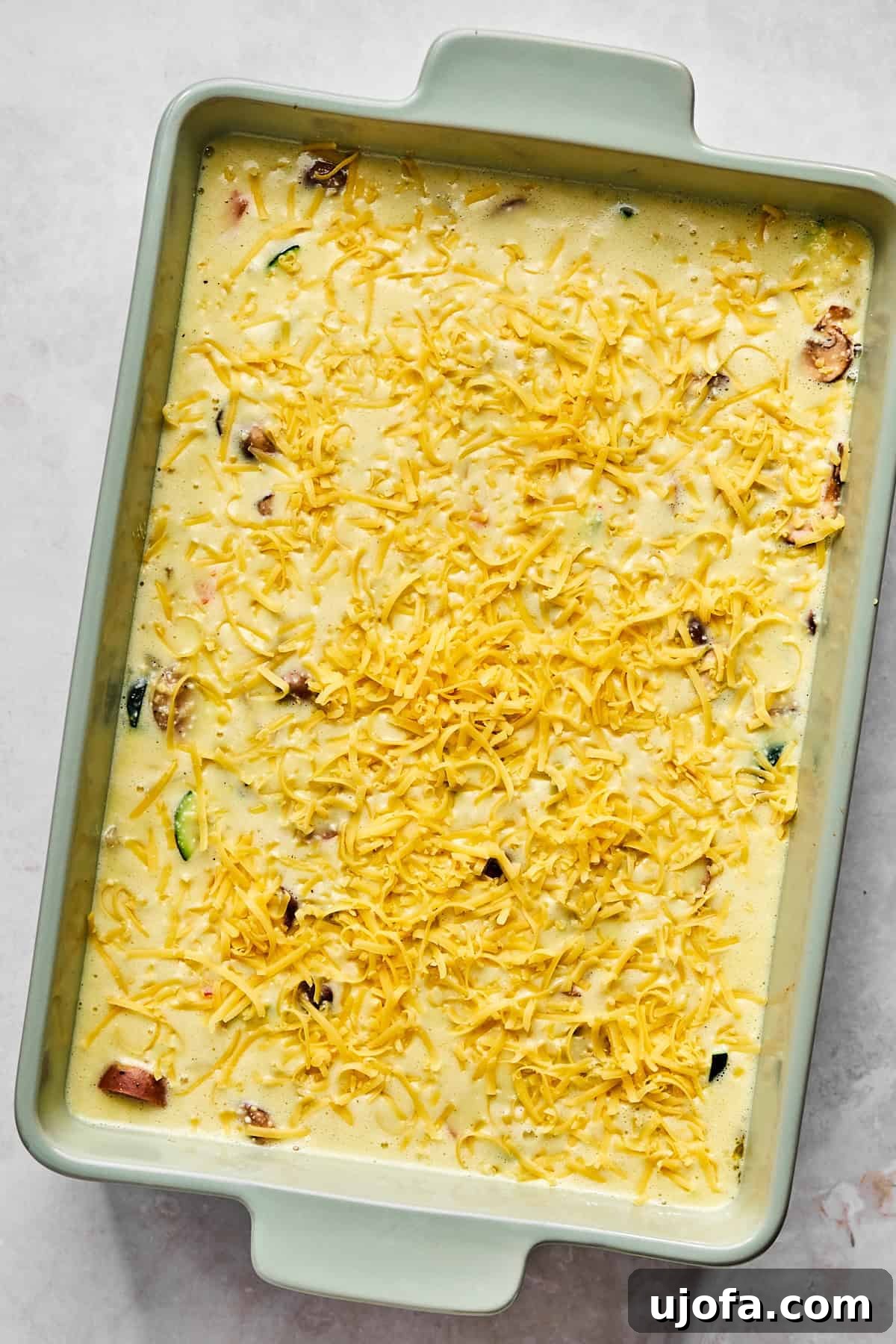 Hearty Cottage Cheese and Chicken Sausage Brunch Bake 8 Unbaked egg casserole sprinkled with cheddar cheese, ready to go into the oven