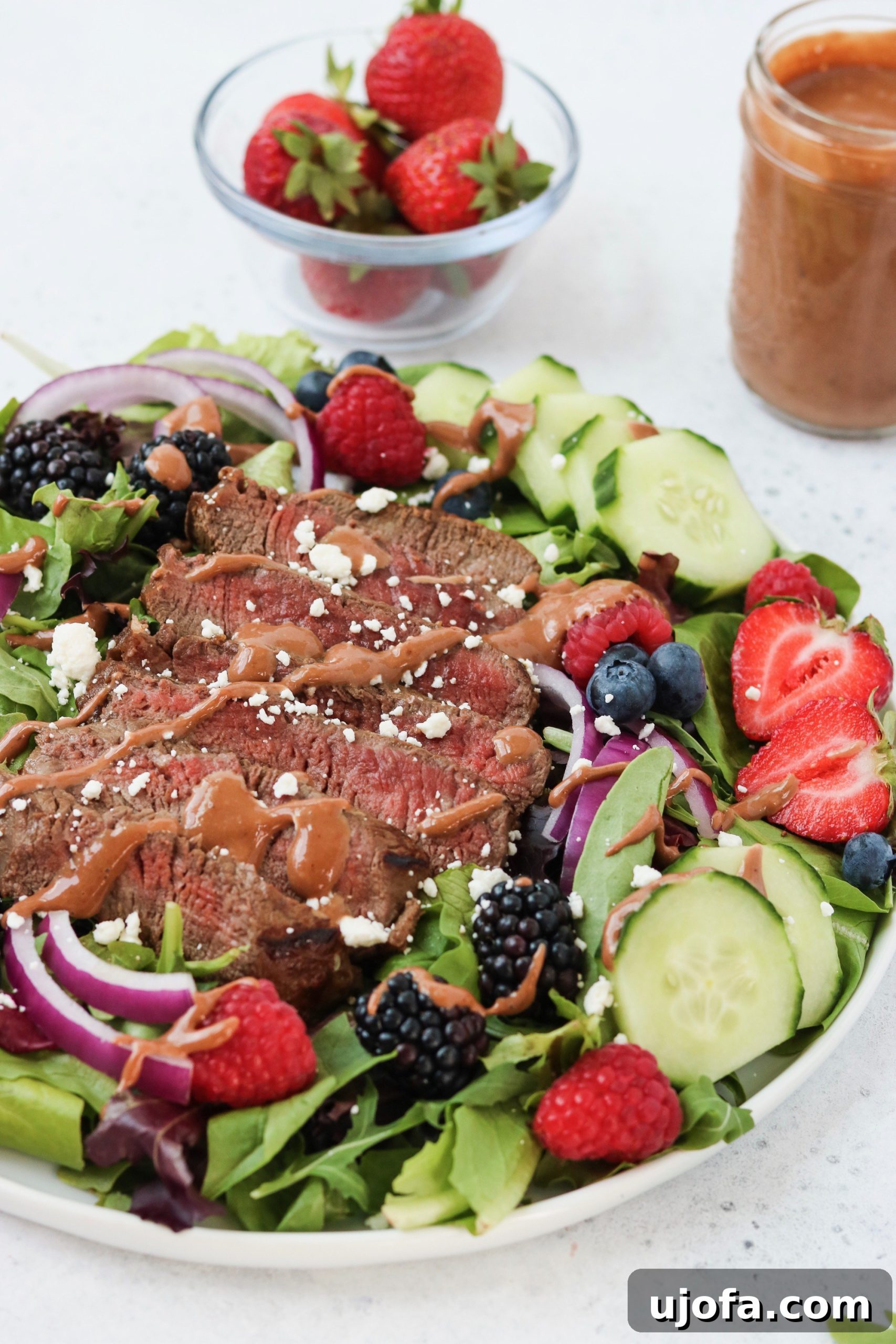 A vibrant salad featuring sliced grilled tenderloin, fresh strawberries, blueberries, and mixed greens, drizzled with a rich strawberry balsamic vinaigrette.