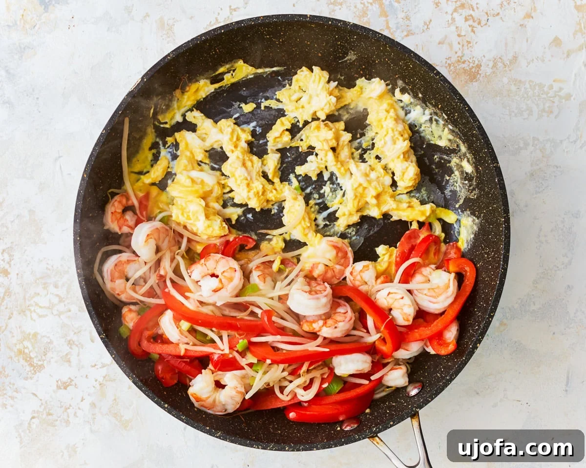 Lightly beaten eggs cooking in an empty section of a skillet with vegetables and shrimp pushed aside.