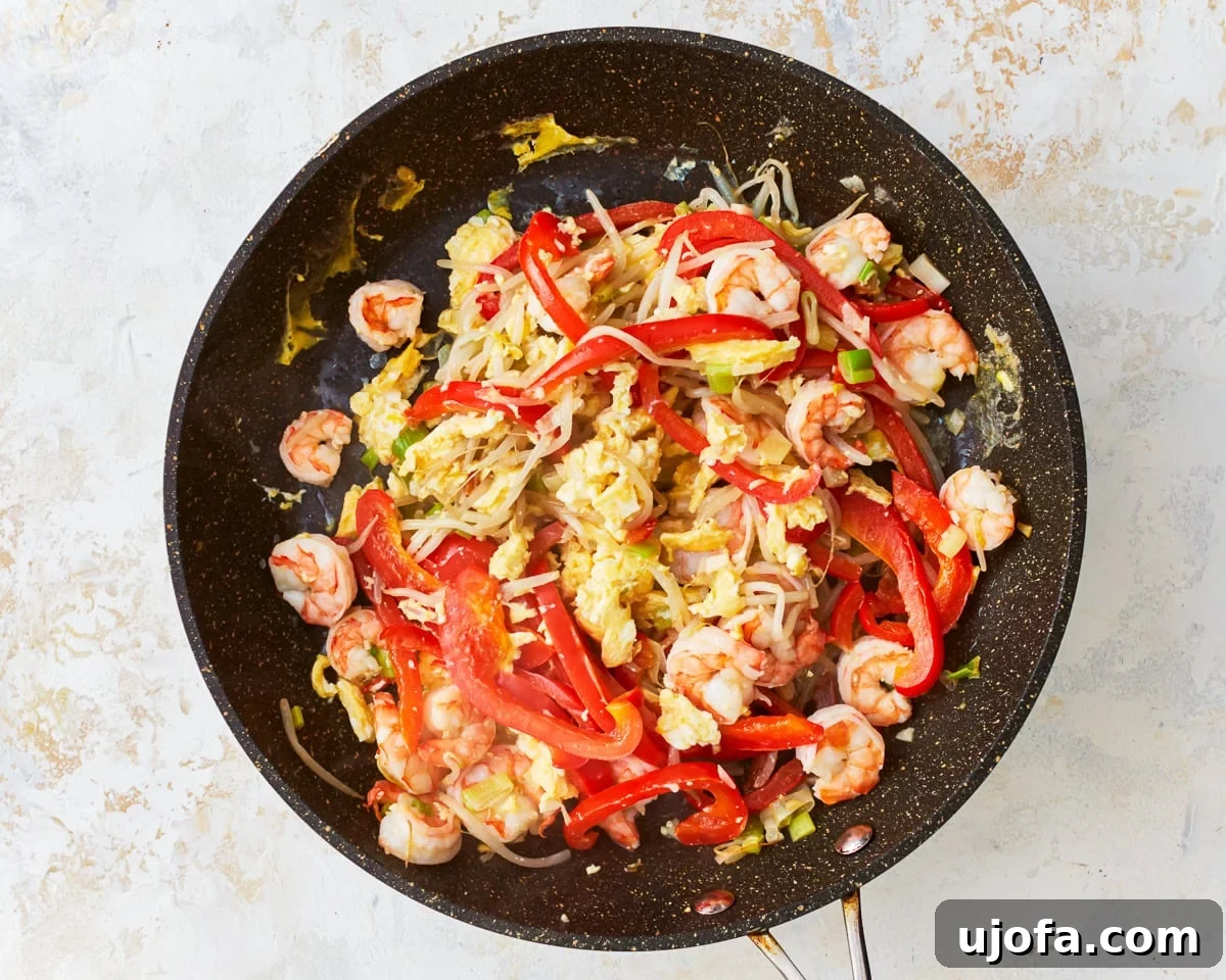 Scrambled eggs mixed with vegetables and shrimp in a skillet.