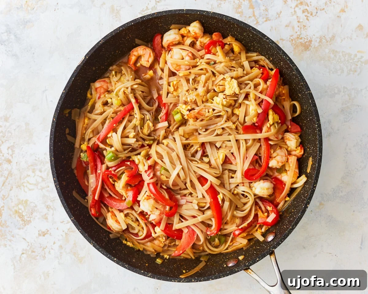 Gluten-free pad thai noodles and ingredients coated in sauce within a skillet.