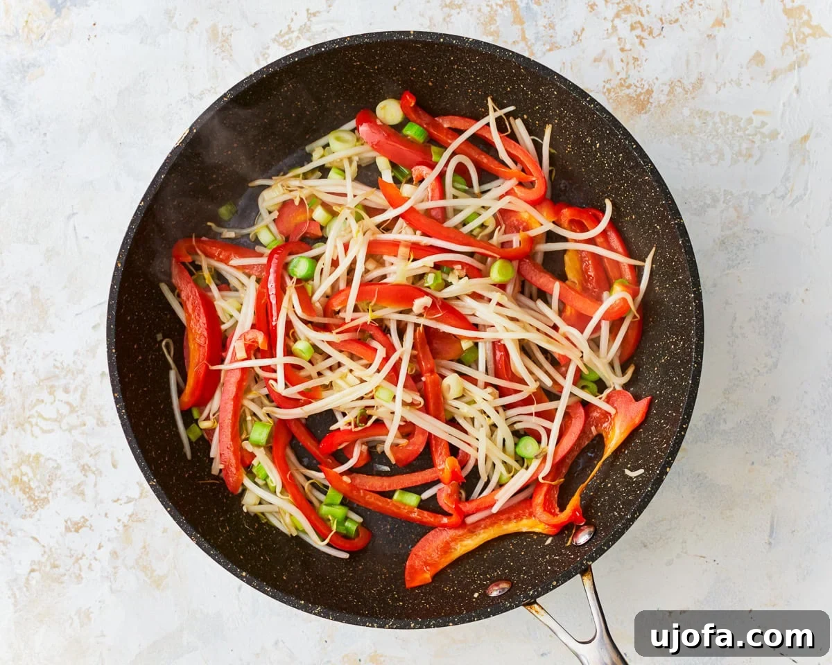 Fresh bean sprouts, bell pepper, green onions, and minced garlic sizzling in a skillet.